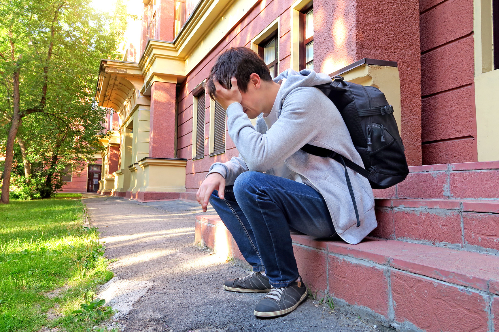 Sad Young Man with Knapsack on the Porch of the House